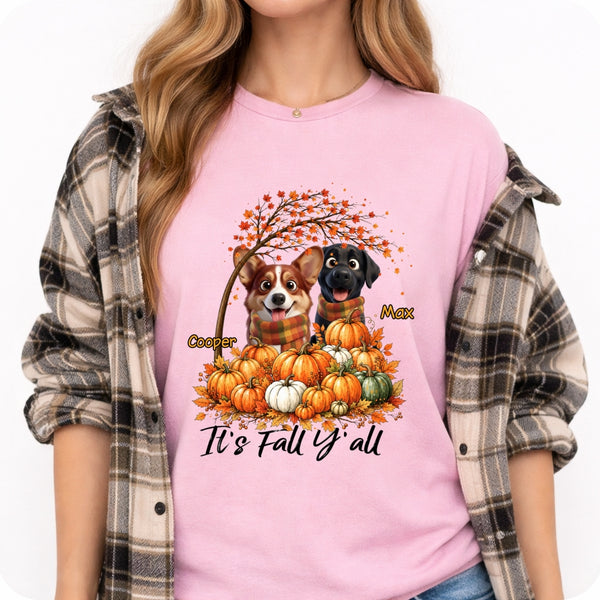A woman wearing a light pink graphic t-shirt with a fall-themed design of two dogs and pumpkins, styled with an open brown and gray plaid flannel shirt over her shoulders.