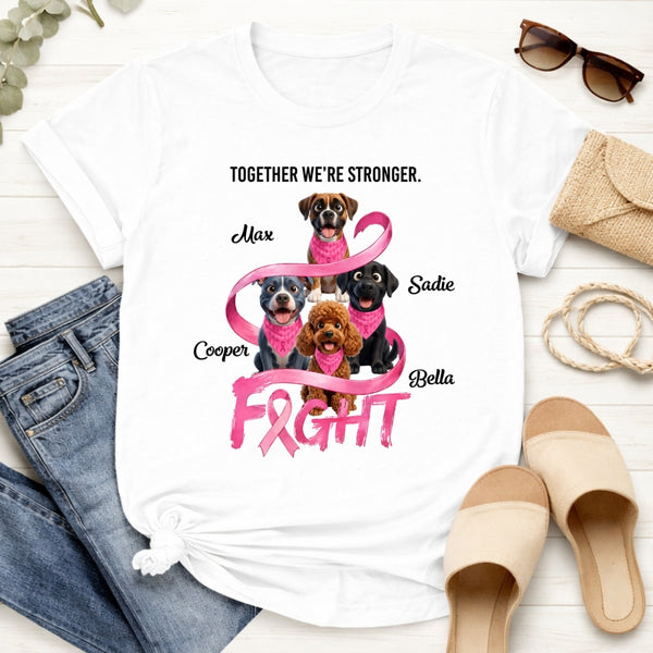 A white graphic T-shirt laid flat on a light wood surface, styled with jeans, sunglasses, a clutch, and sandals. The shirt features a pink ribbon design with four dogs and the text 'TOGETHER WE'RE STRONGER.