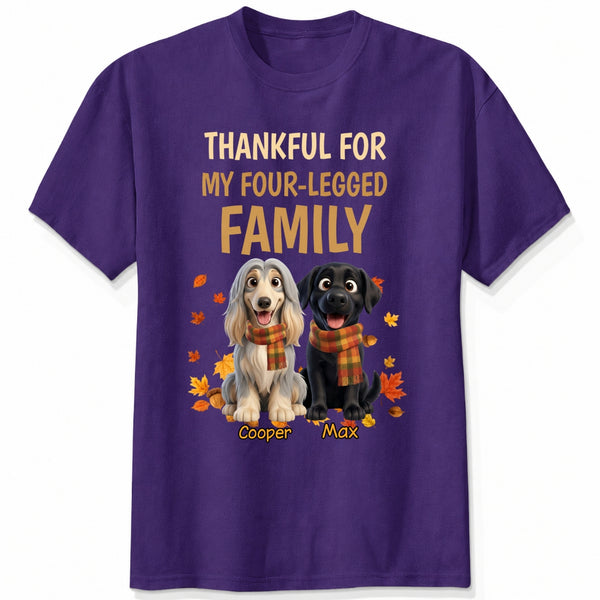 A purple short-sleeve crewneck t-shirt with a graphic print. The print features the text 'THANKFUL FOR MY FOUR-LEGGED FAMILY' in beige and orange lettering, above an illustration of custom dogs wearing orange plaid scarves, surrounded by autumn leaves. customized with dog's names