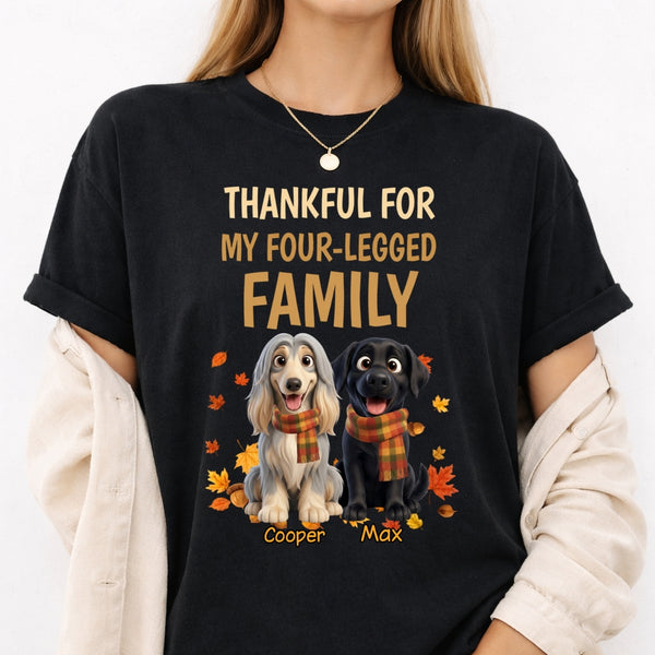 A woman wearing a black graphic t-shirt with a custom design that reads 'THANKFUL FOR MY FOUR-LEGGED FAMILY' above two dogs, wearing orange plaid scarves with autumn leaves. She has a cream-colored cardigan draped off her shoulders.
