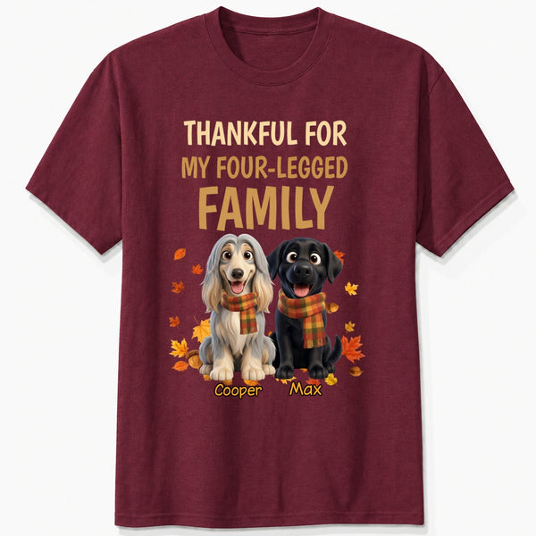 A maroon short-sleeve crewneck t-shirt with a graphic print. The print features the text 'THANKFUL FOR MY FOUR-LEGGED FAMILY' in beige and orange lettering, above an illustration of custom dogs wearing orange plaid scarves, surrounded by autumn leaves. customized with dog's names