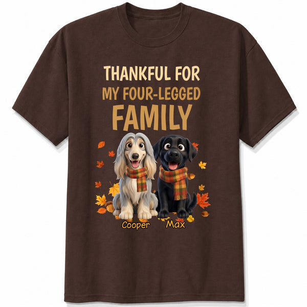 A dark chocolate short-sleeve crewneck t-shirt with a graphic print. The print features the text 'THANKFUL FOR MY FOUR-LEGGED FAMILY' in beige and orange lettering, above an illustration of custom dogs wearing orange plaid scarves, surrounded by autumn leaves. customized with dog's names