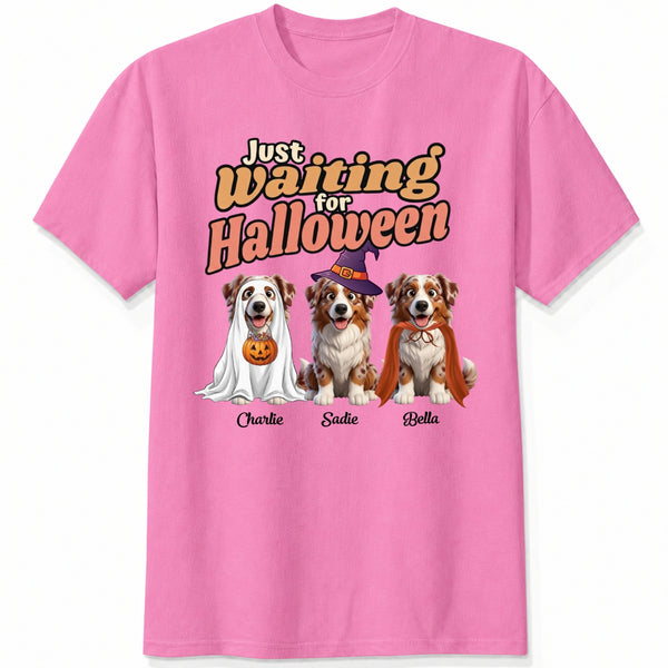 A pink short-sleeve crewneck t-shirt featuring dogs dressed in costumes and the text 'Just Waiting for Halloween'.